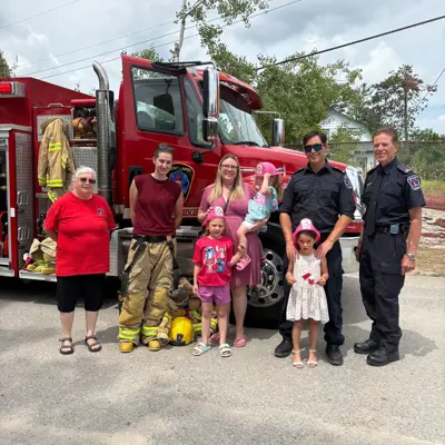 children standing with firefighters in front of firetruck